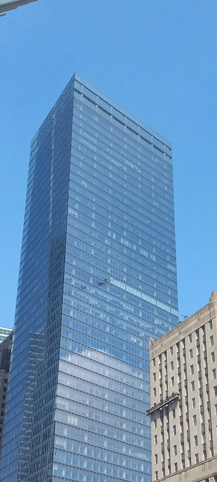 Стеклянная башня 7 World Trade Center на фоне голубого неба рядом со старым каменным зданием