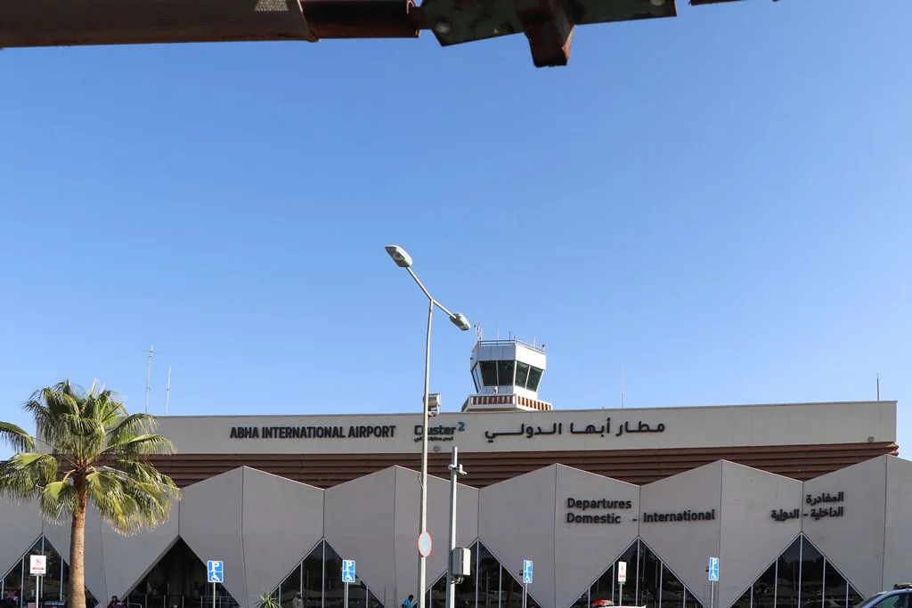 The zigzag facade of the Abha International Airport terminal, the control tower and a palm tree in front