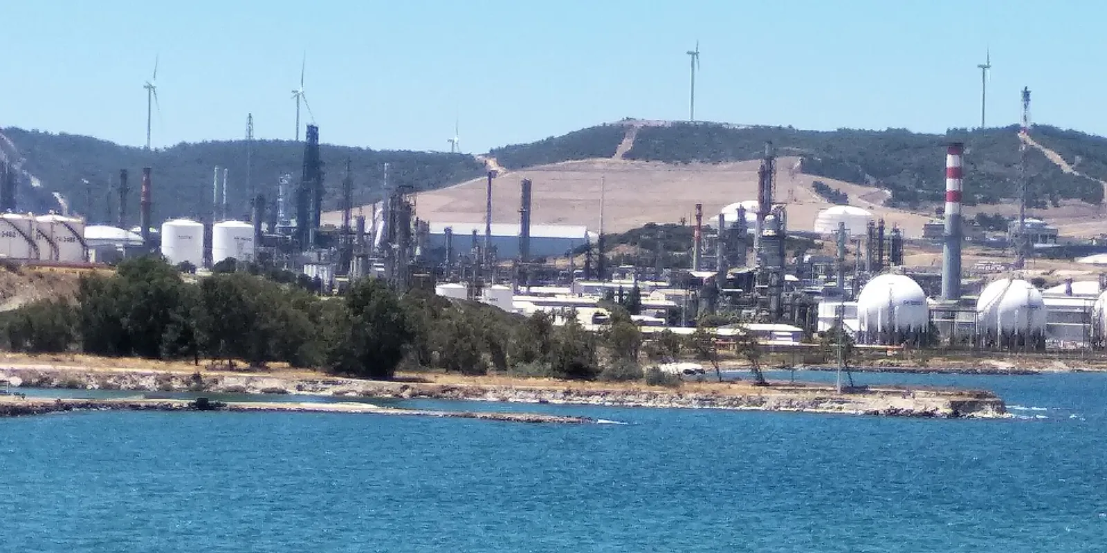 The STAR refinery on the Aegean coast, with stacks, spherical tanks and distillation towers in front of hills lined with wind turbines