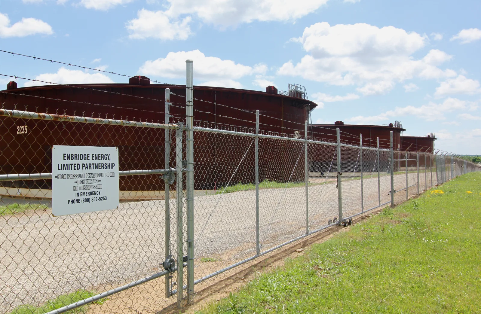 Large crude oil storage tanks lined up behind a barbed-wire fence in Cushing, Oklahoma, United States