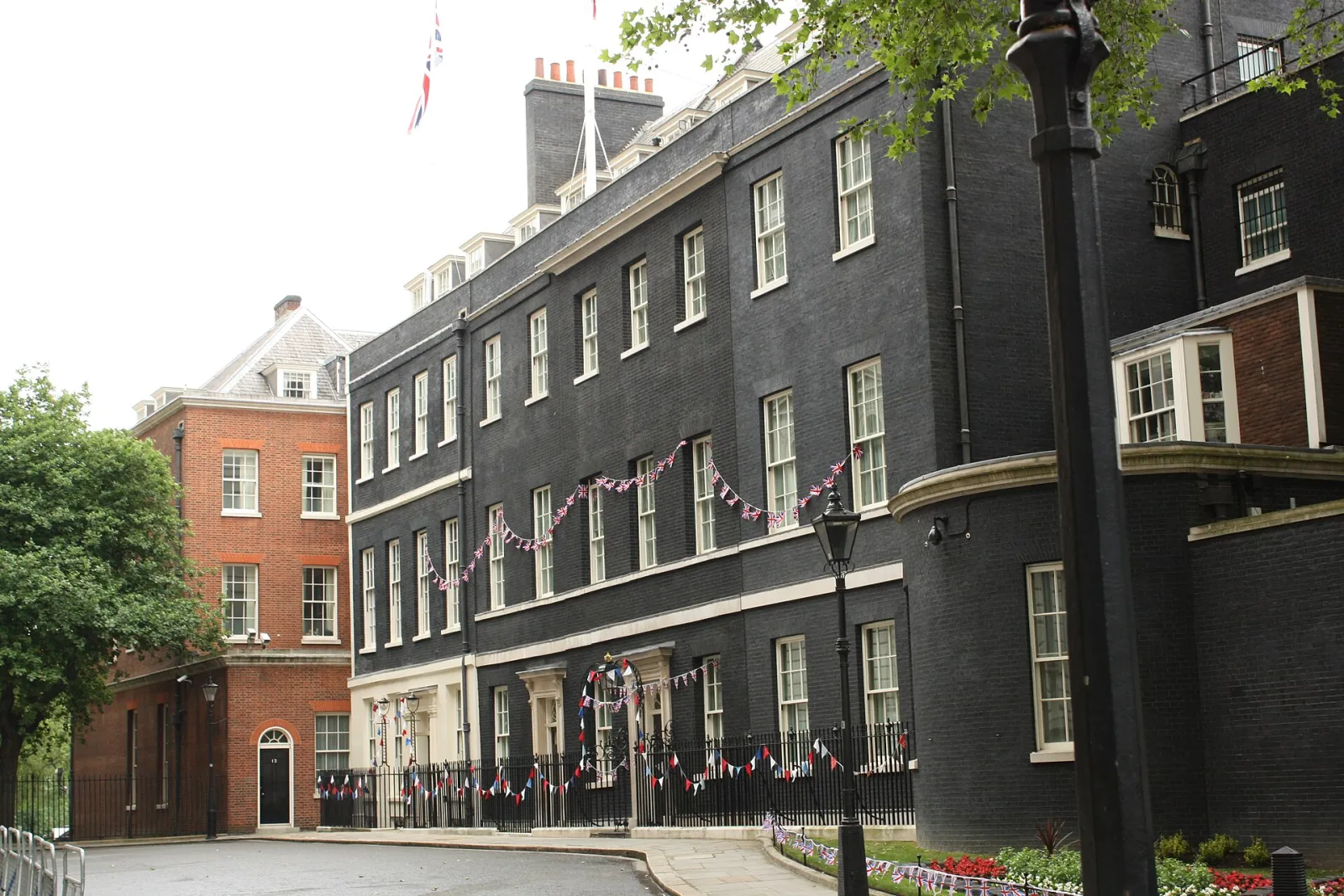 Londra'da Downing Street'te koyu tuğla cepheli bitişik konutlar, demir parmaklıklar ve bayrak süsleri