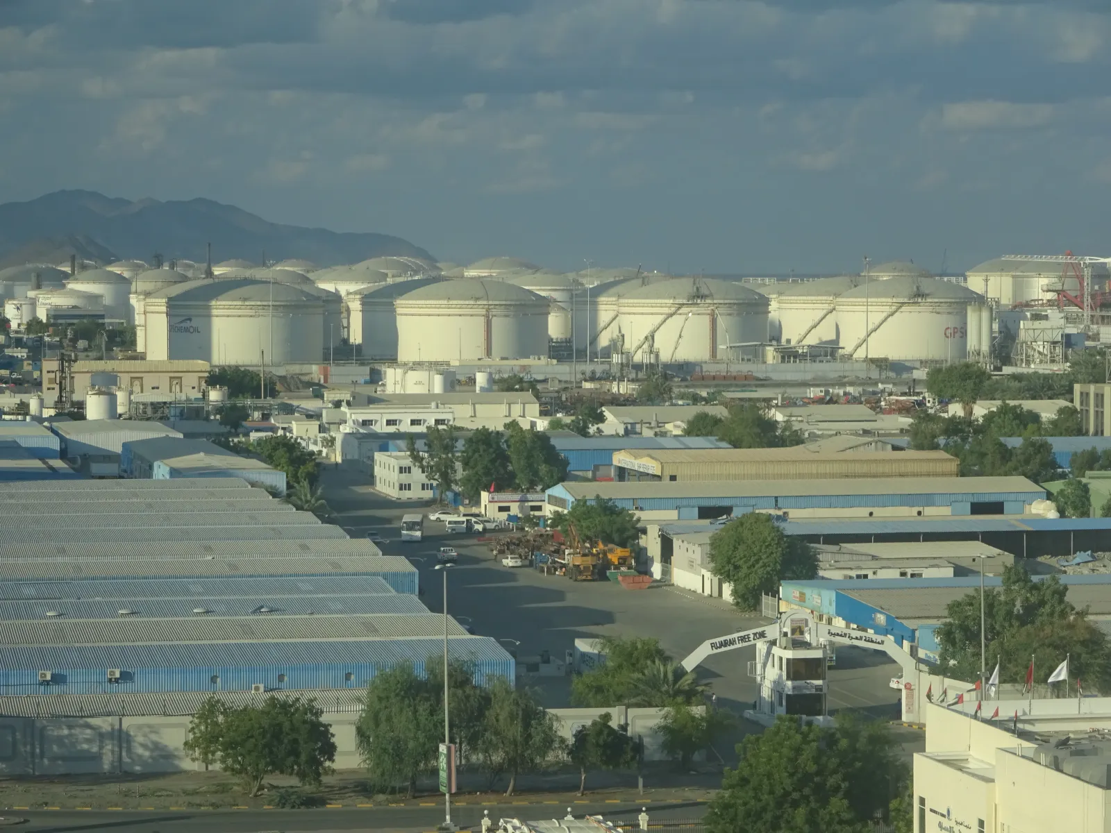 Rows of large white oil storage tanks near the Port of Fujairah, with port buildings in the foreground