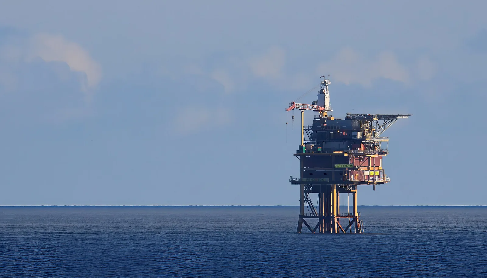 An orange-and-white oil production platform standing alone on the horizon of the open sea