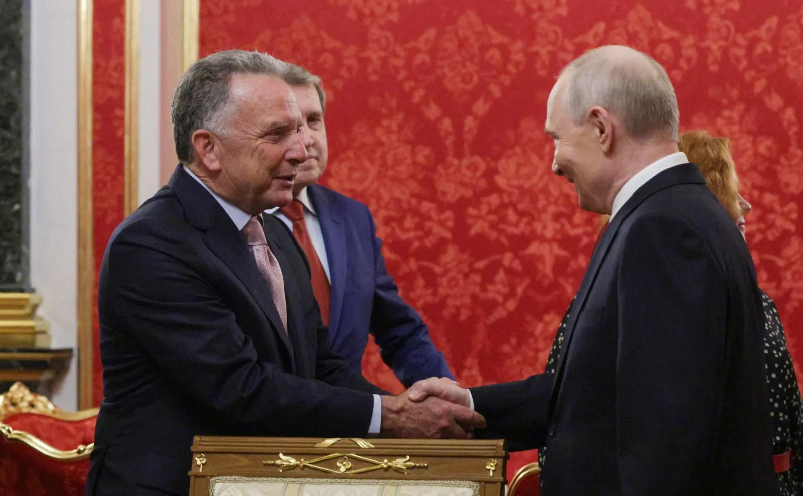 Vladimir Putin and Steve Witkoff shake hands in a Kremlin hall with red damask walls