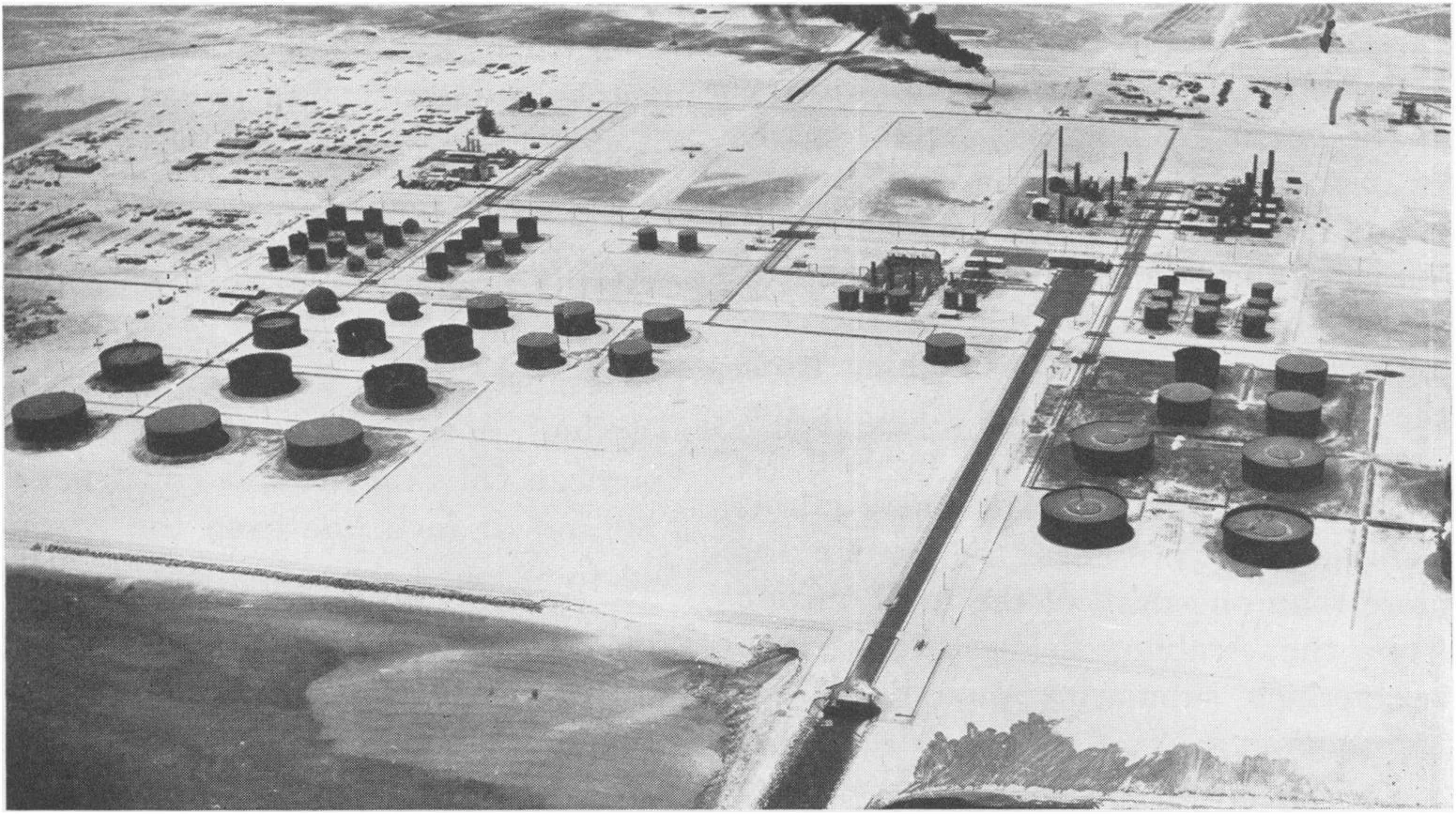 Aerial black-and-white view of the Ras Tanura refinery and oil storage tanks on Saudi Arabia's Gulf coast