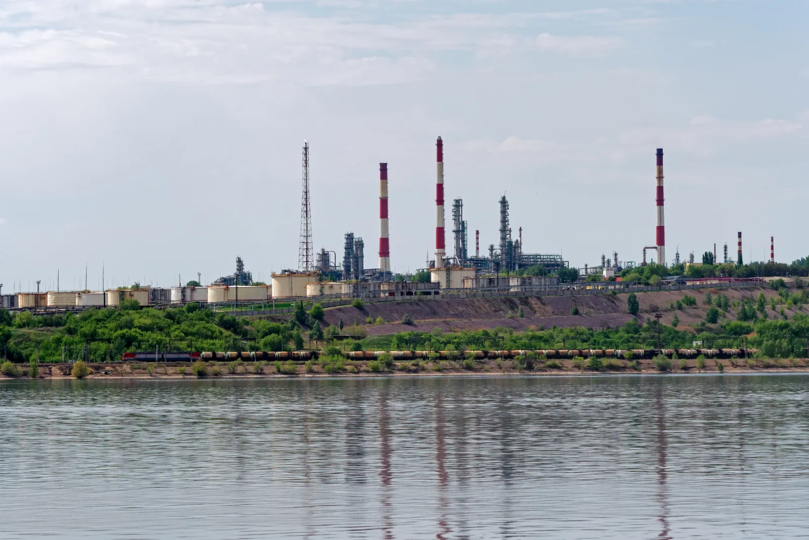 Chimneys and storage tanks of the Saratov refinery on the Volga, with a train of fuel tank cars passing below