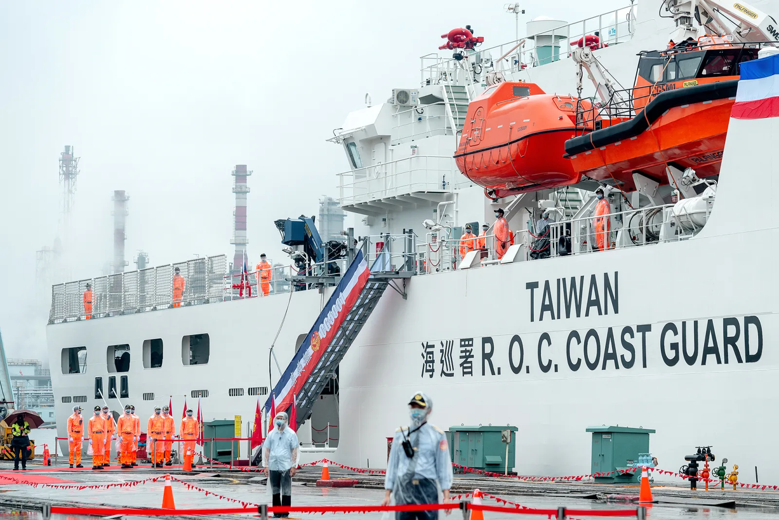 A white patrol vessel marked "TAIWAN R.O.C. COAST GUARD" at the quay, crew in orange overalls lined up on deck