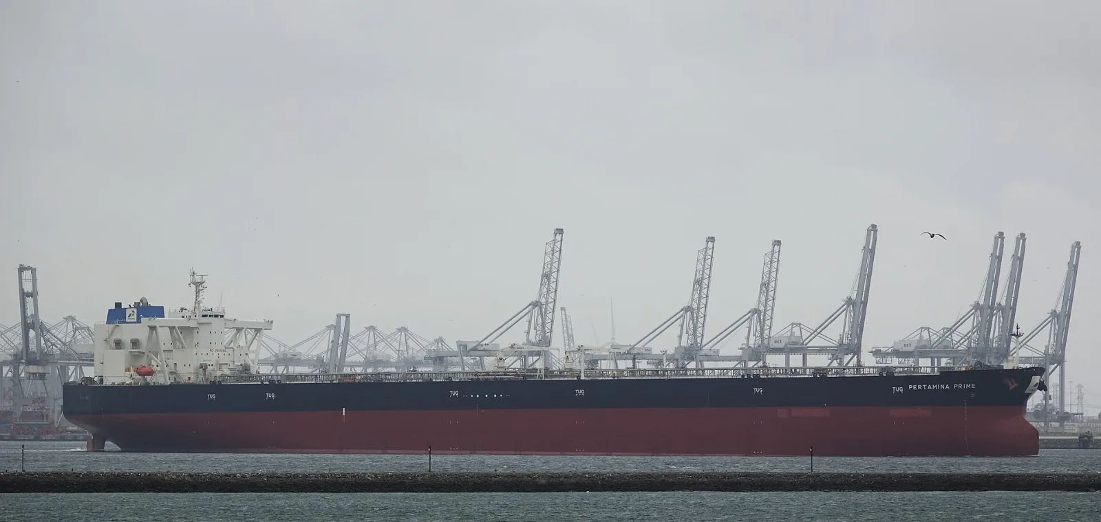 An unladen very large crude carrier riding high with its red lower hull exposed, port cranes behind